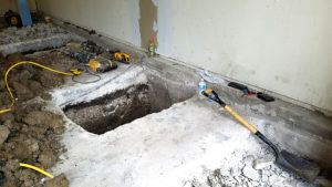 Hole dug into concrete with various tools around it