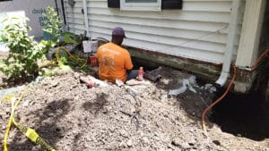 Man installing foundation piers in hole near house