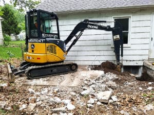 Backhoe digging up dirt near house wall