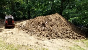 Large pile of dirt and backhoe near woods