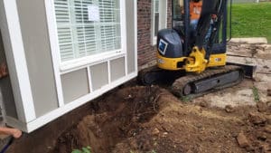 Backhoe digs hole near foundation of house