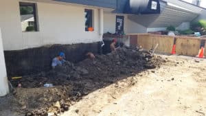 Men digging ditch next to outside wall