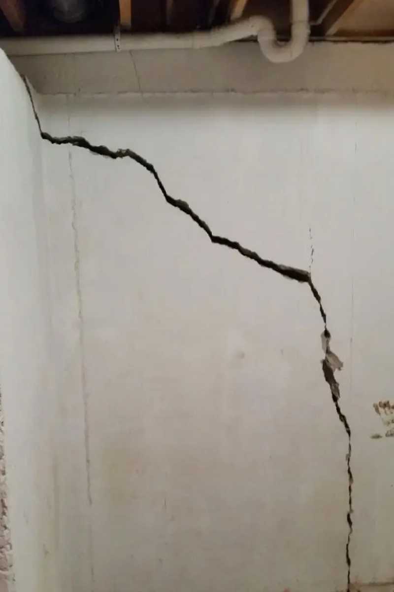 Close-up of a large vertical crack running through an interior concrete foundation wall