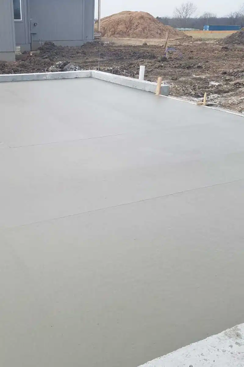New concrete foundation slab poured at a construction site with dirt piles nearby