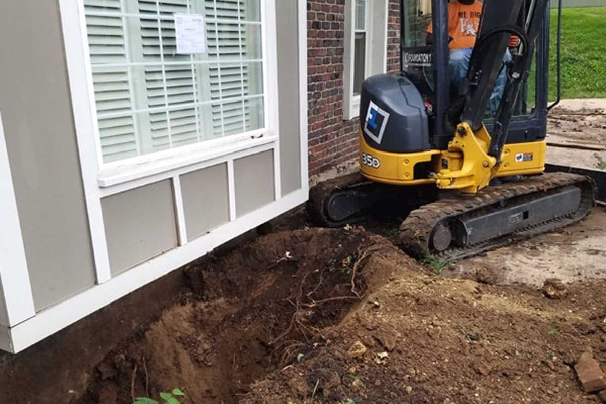 Excavator digging alongside a newly poured foundation wall with window well framing visible