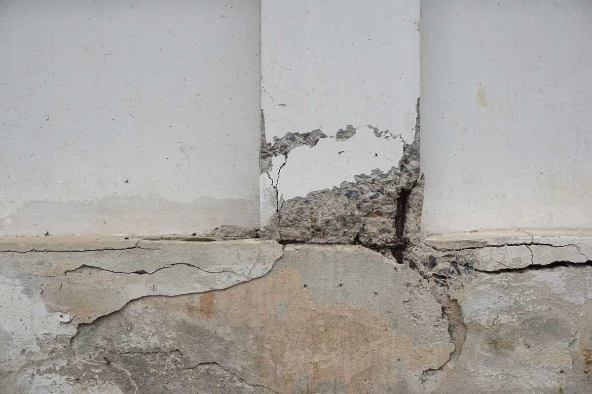 Severely damaged foundation wall with large cracks, crumbling concrete, and exposed material.