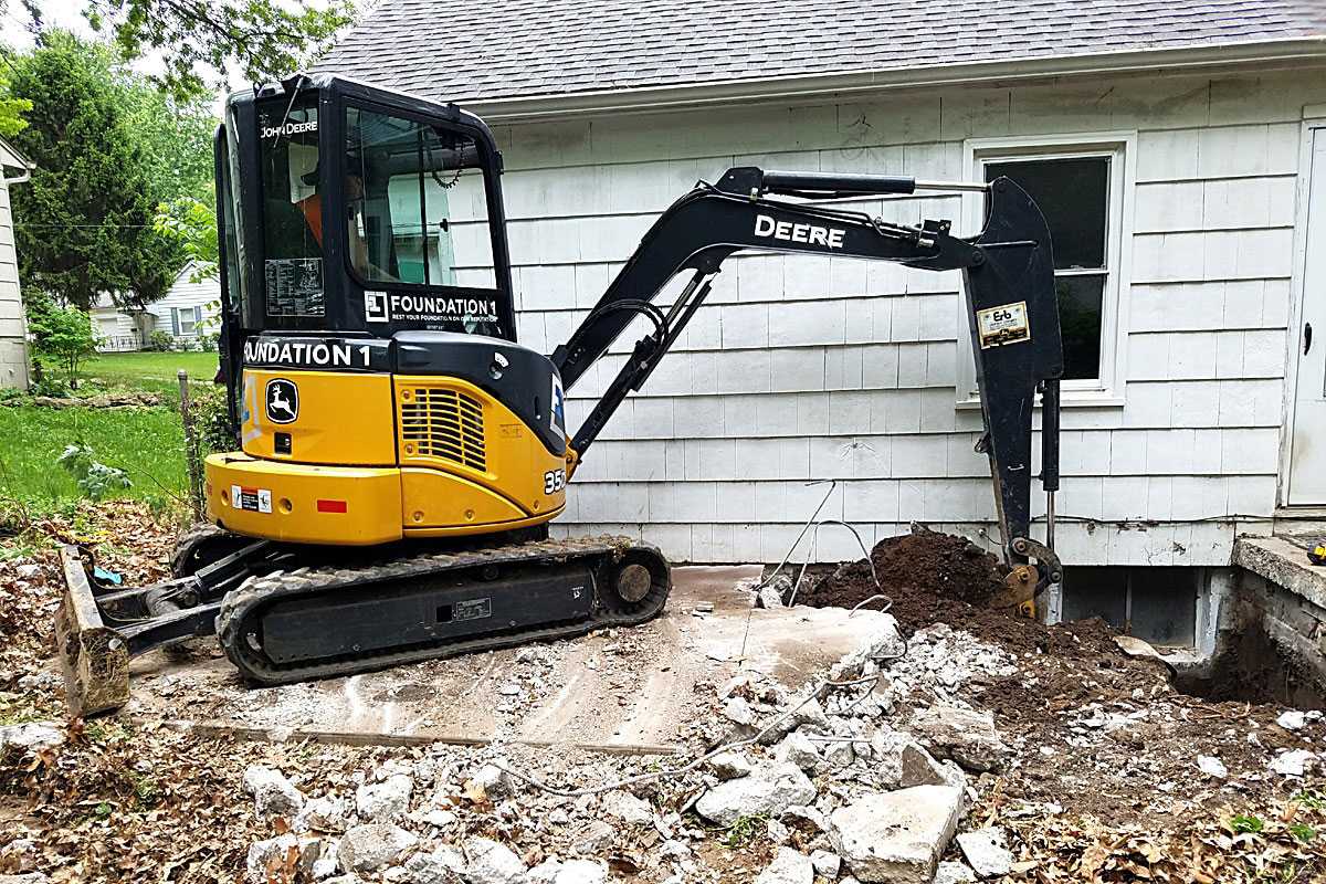 Excavator digging alongside a home foundation for repair in Gladstone